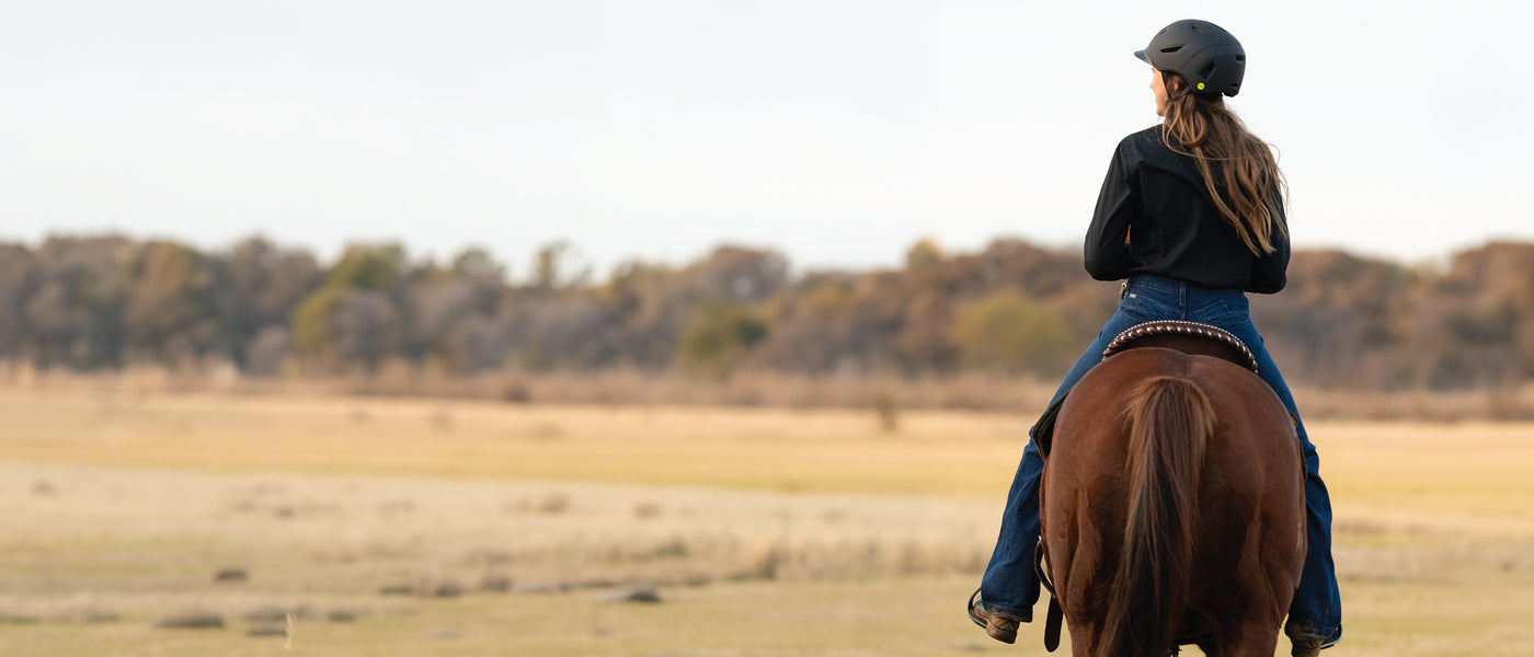Rider wearing a black helmet riding a brown horse across an open field.